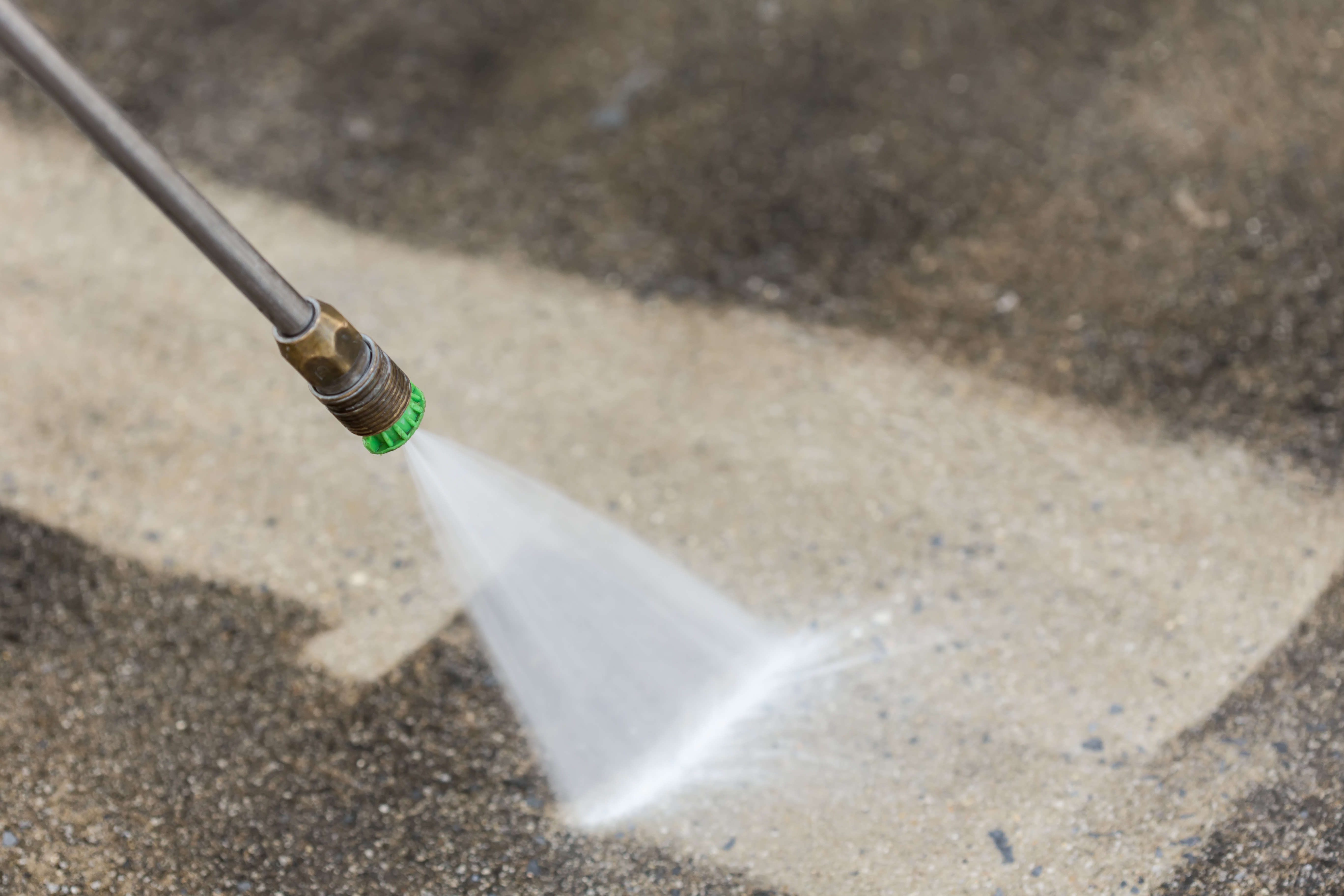 Pressure washer nozzle spraying water on concrete surface